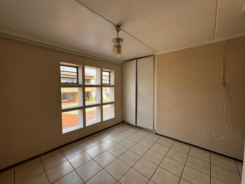 An empty bedroom featuring tiled flooring, a built-in wardrobe, and a distinctive grid-style window providing natural light.