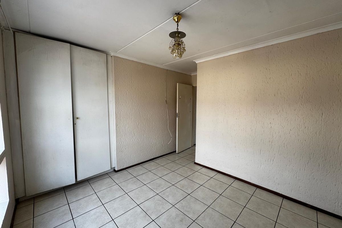 An empty bedroom featuring tiled flooring, built-in cupboards, and a classic ceiling light fixture, requiring minor cosmetic updates.