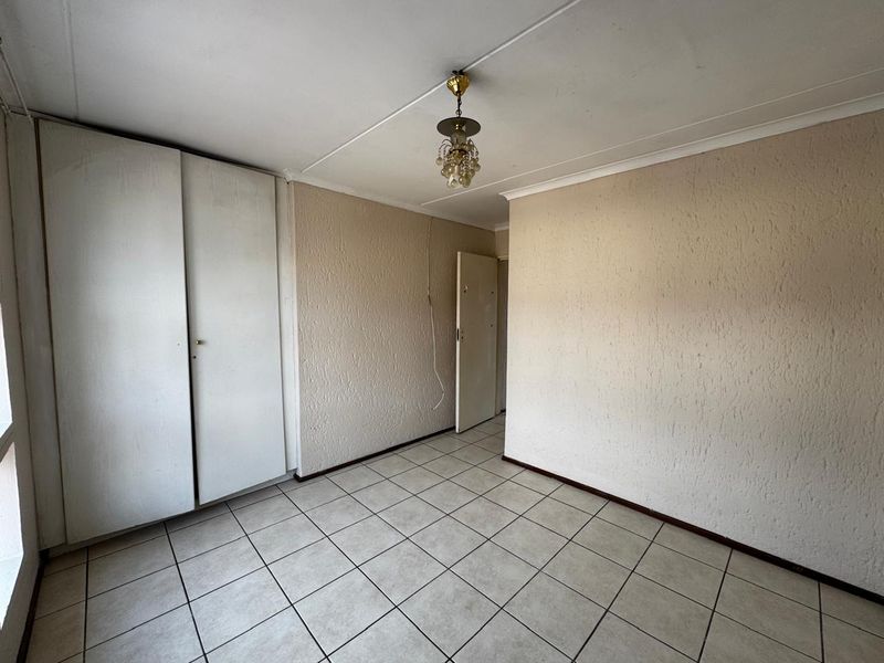 An empty bedroom featuring tiled flooring, built-in cupboards, and a classic ceiling light fixture, requiring minor cosmetic updates.