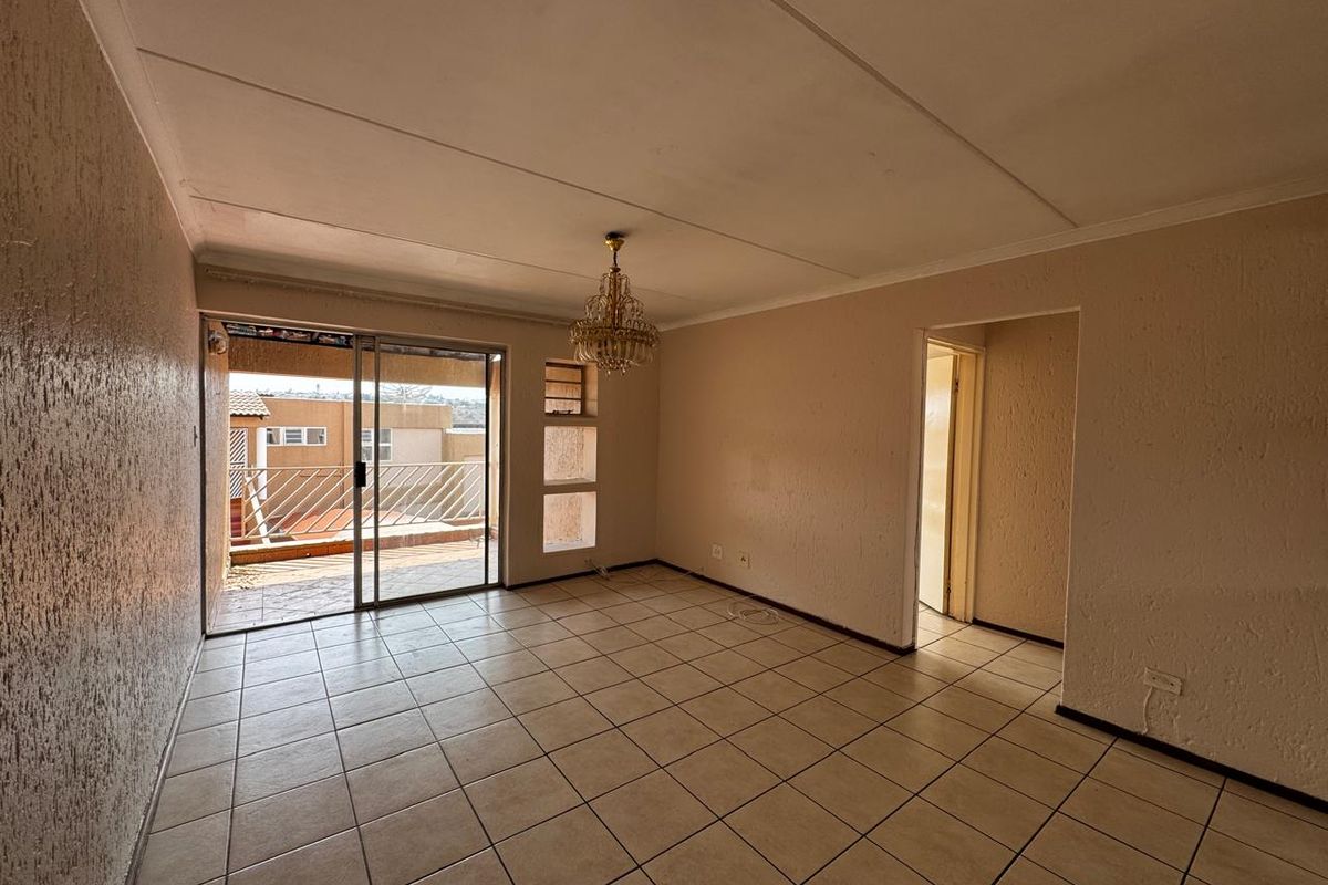 An empty living room featuring tiled flooring, textured walls, and a sliding glass door leading to an outdoor balcony area.
