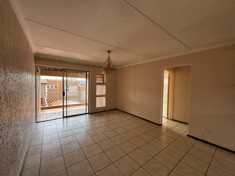 An empty living room featuring tiled flooring, textured walls, and a sliding glass door leading to an outdoor balcony area.