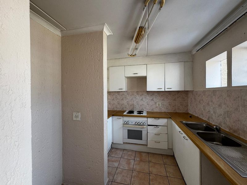 A dated kitchen featuring white cabinetry, laminate countertops, a built-in oven and hob, and tiled flooring, offering potential for a modern renovation.