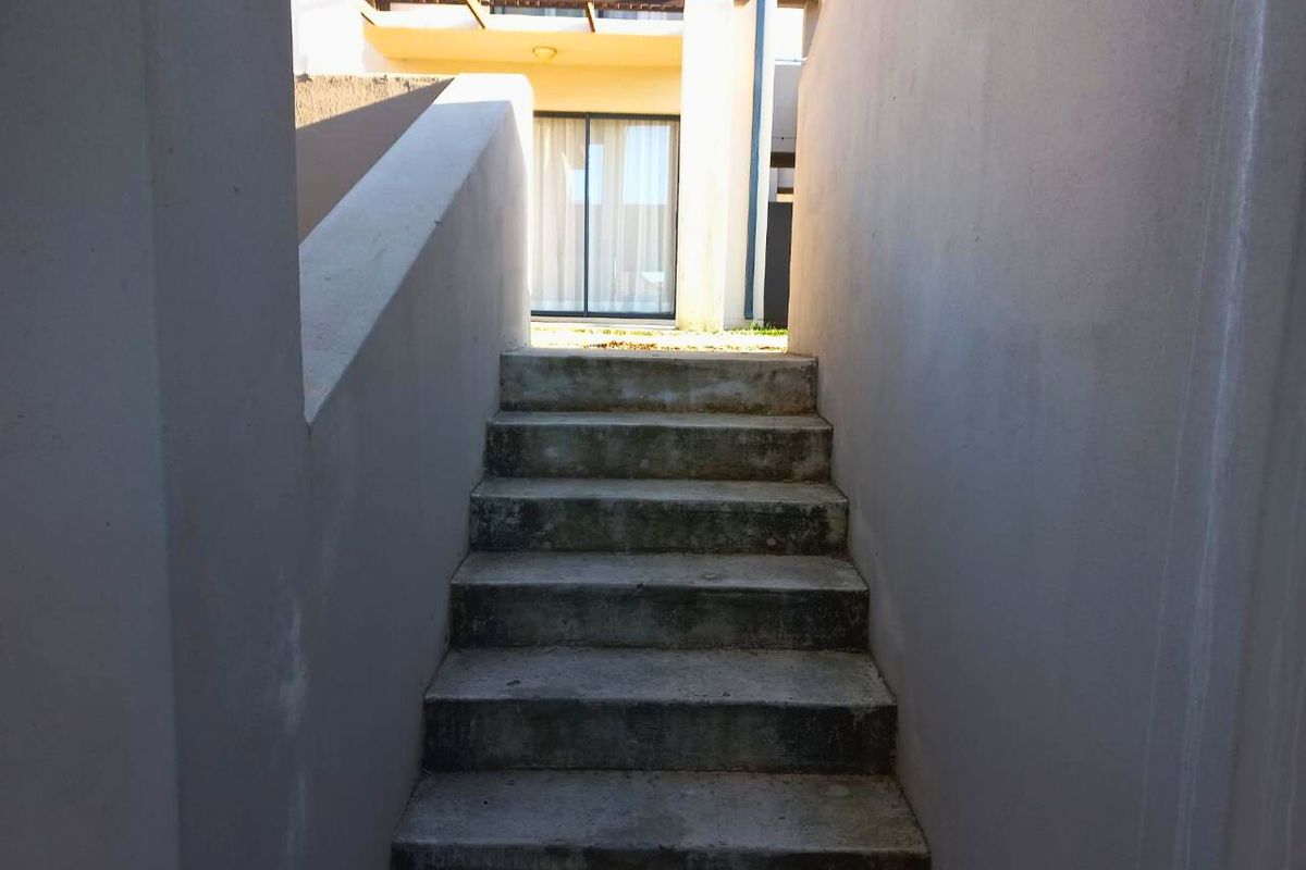 Exterior view of a concrete staircase leading to a rear apartment entrance with a sliding glass door and upper balcony.