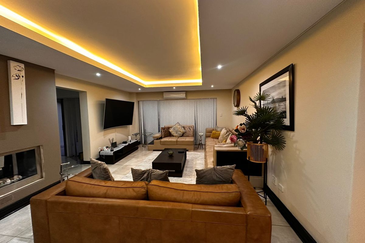 Spacious living room featuring a modern recessed ceiling with ambient cove lighting, tiled flooring, and a built-in fireplace.