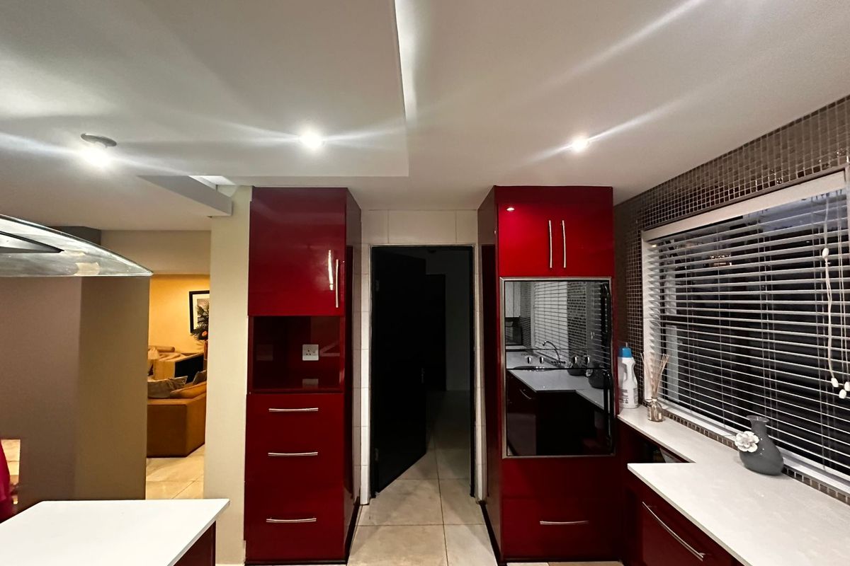 Modern kitchen featuring high-gloss red cabinetry, stone countertops, and a mosaic tile backsplash with integrated built-in oven and recessed lighting.