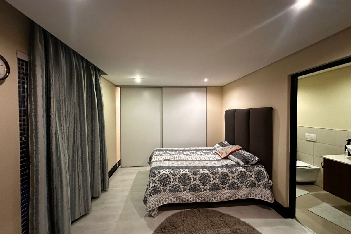 Spacious bedroom featuring neutral tones, built-in sliding door wardrobes, recessed lighting, and direct access to an en-suite bathroom.