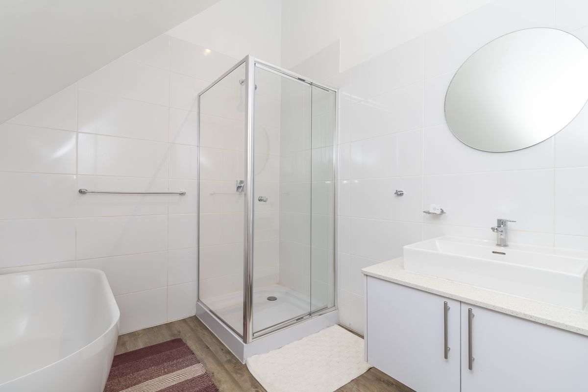 A clean, modern bathroom featuring a glass shower enclosure, a white vanity with basin, and a freestanding bathtub against tiled walls.