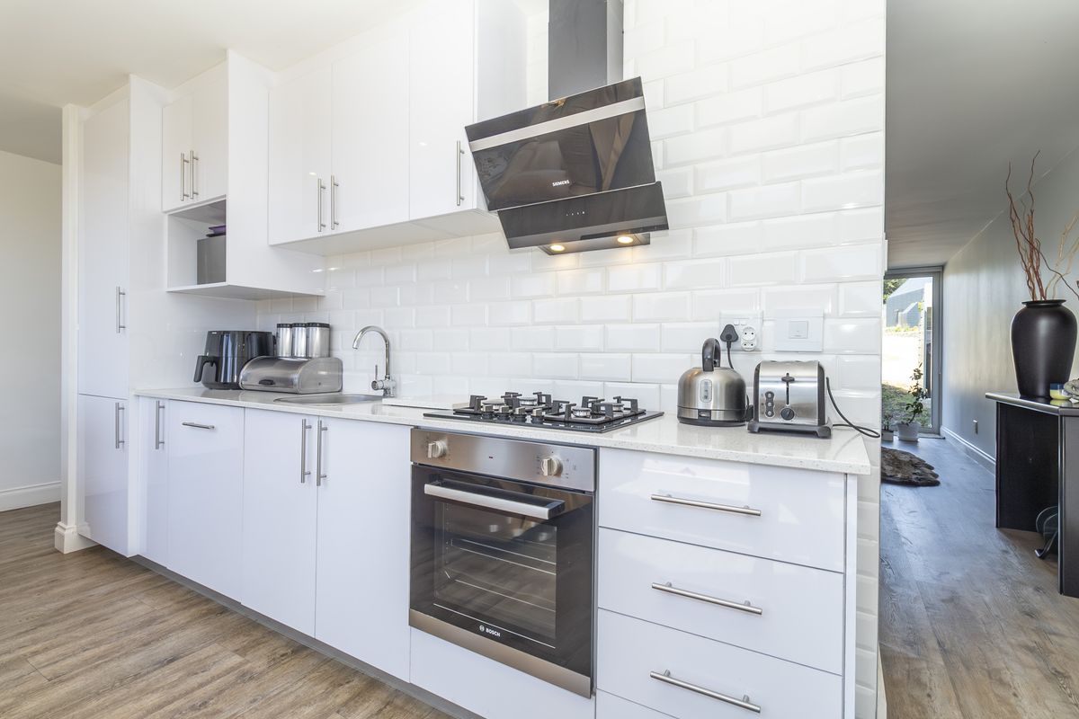 Modern kitchen featuring white gloss cabinetry, subway tile backsplash, stone countertops, and integrated stainless steel appliances including a gas hob and oven.