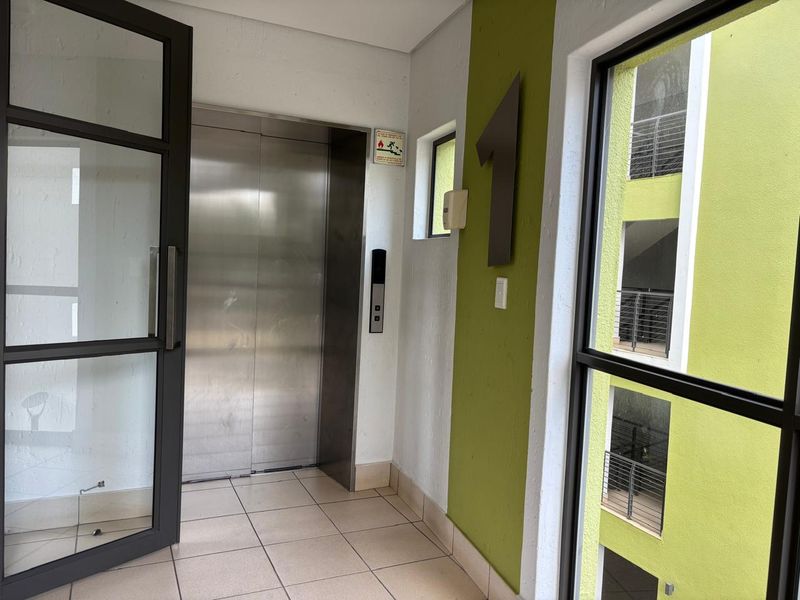 A clean and modern apartment building elevator lobby featuring tiled floors, a stainless steel elevator, and large unit number signage.