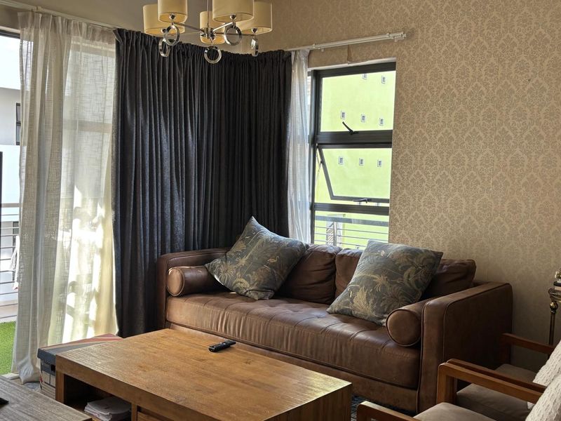 A cozy living room featuring patterned wallpaper, a modern chandelier, and large windows allowing natural light, providing a comfortable and inviting atmosphere.