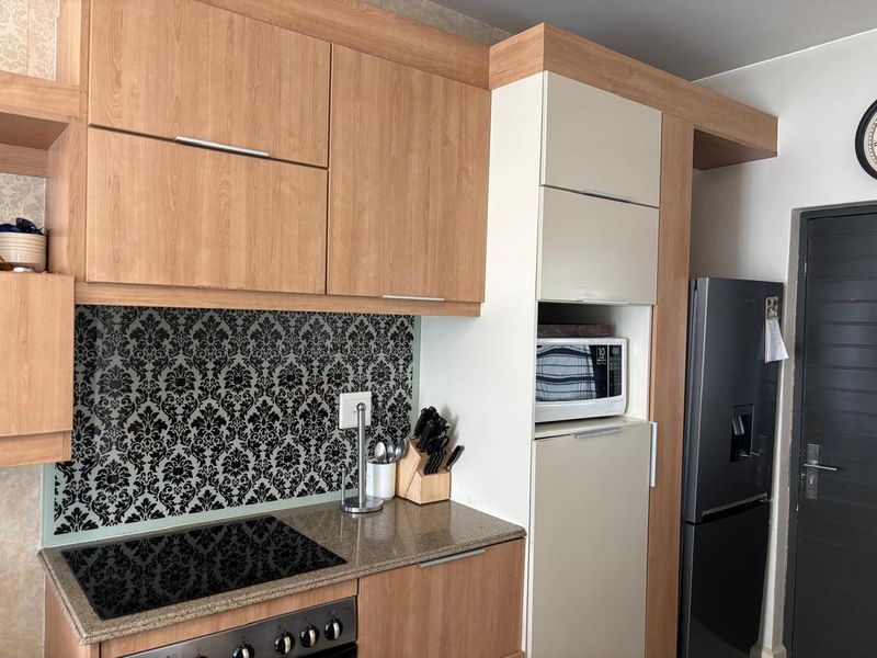 A compact kitchen featuring wood-tone cabinetry, stone countertops, a patterned backsplash, and integrated appliances including a hob and microwave.