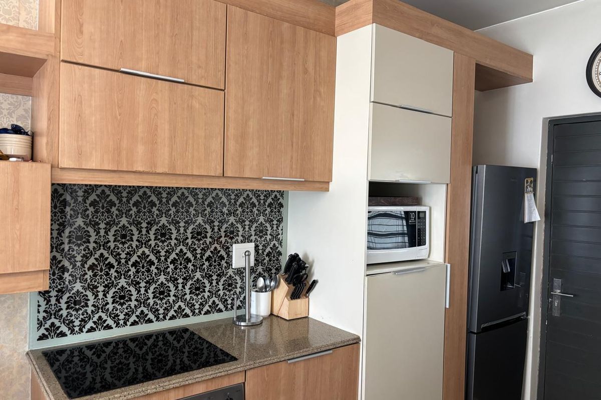 A compact kitchen featuring wood-tone cabinetry, stone countertops, a patterned backsplash, and integrated appliances including a hob and microwave.