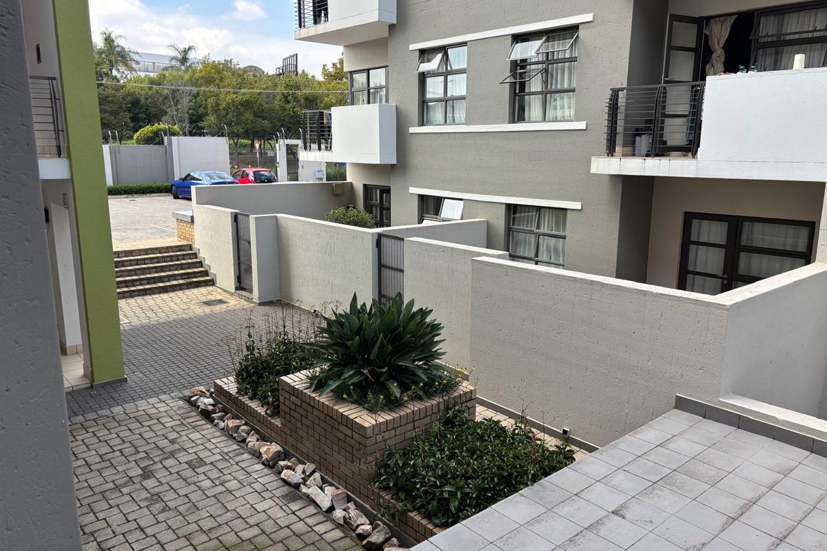 A view of the apartment complex rear exterior, featuring paved courtyard areas, brick planter boxes, and private balconies with metal railings.