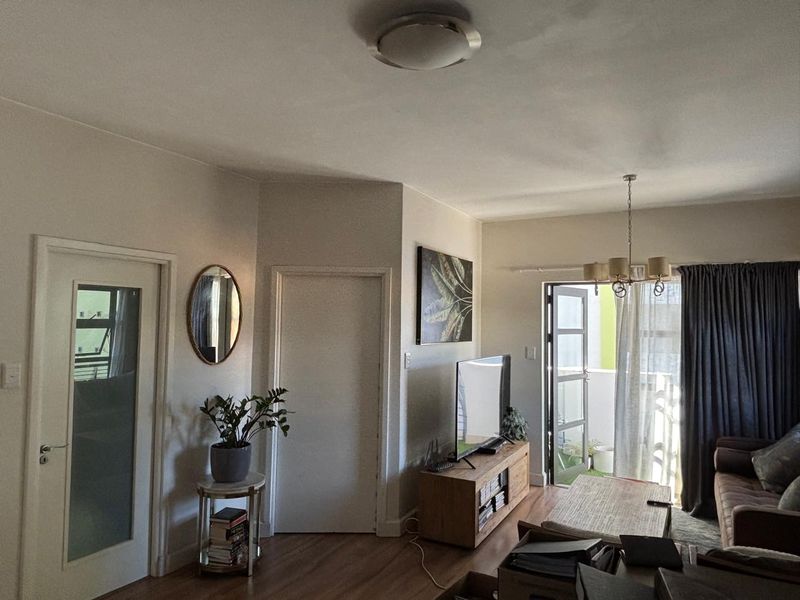 A comfortable living room featuring laminate flooring, a chandelier, and direct access to a private balcony through a glass door.