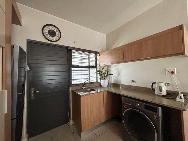 Functional laundry area featuring built-in wooden cabinetry, stone countertops, a stainless steel sink, and dedicated plumbing connections for a washing machine.