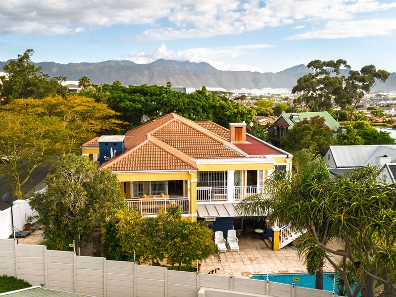 Aerial view of a two-story residential property featuring a terracotta roof, balcony, paved patio area, and a swimming pool set against a mountain backdrop.
