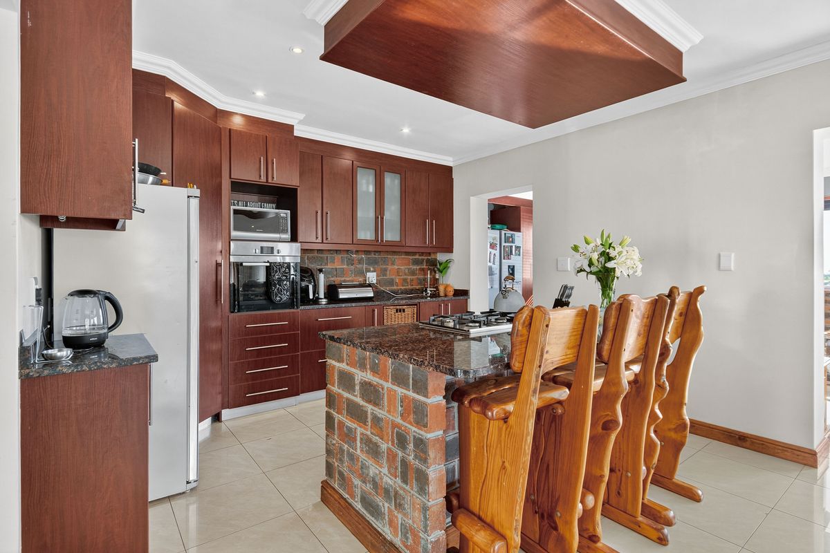 A well-appointed kitchen featuring dark wood cabinetry, granite countertops, a brick-base island with a gas hob, and a modern bulkhead ceiling design.
