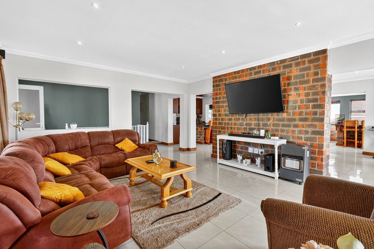 Spacious living room featuring a prominent exposed brick wall, neutral tiled flooring, and recessed lighting, creating a warm and inviting atmosphere.