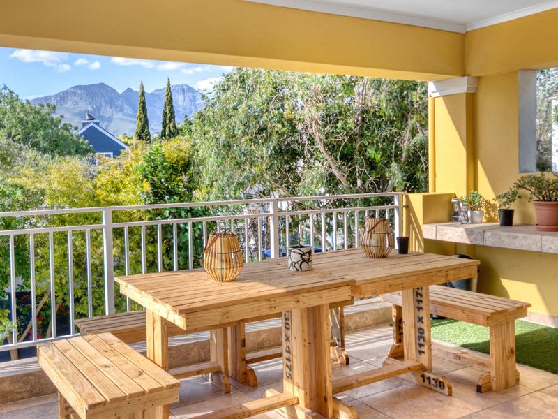 A covered balcony featuring tiled flooring, a built-in stone counter, and a white metal balustrade, offering scenic mountain views.