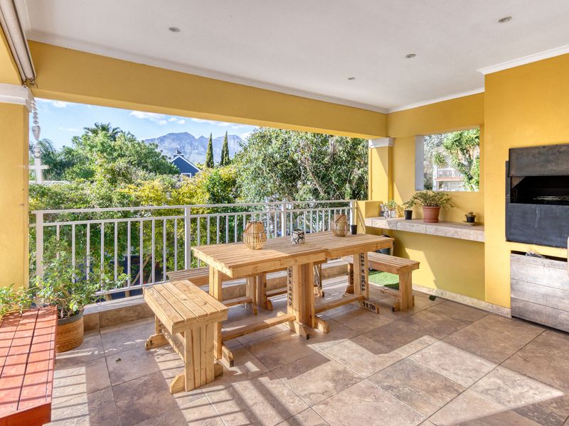 Covered patio featuring a built-in braai, stone prep counter, tiled flooring, and a metal balustrade overlooking the garden and mountain views.