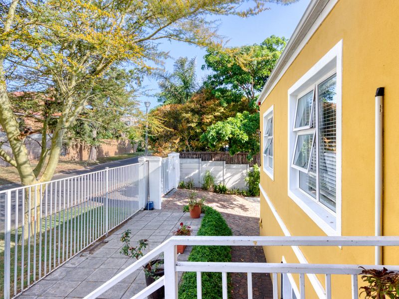 A view of the front exterior featuring a paved walkway, metal fencing, and a brick driveway alongside the yellow-painted building facade.