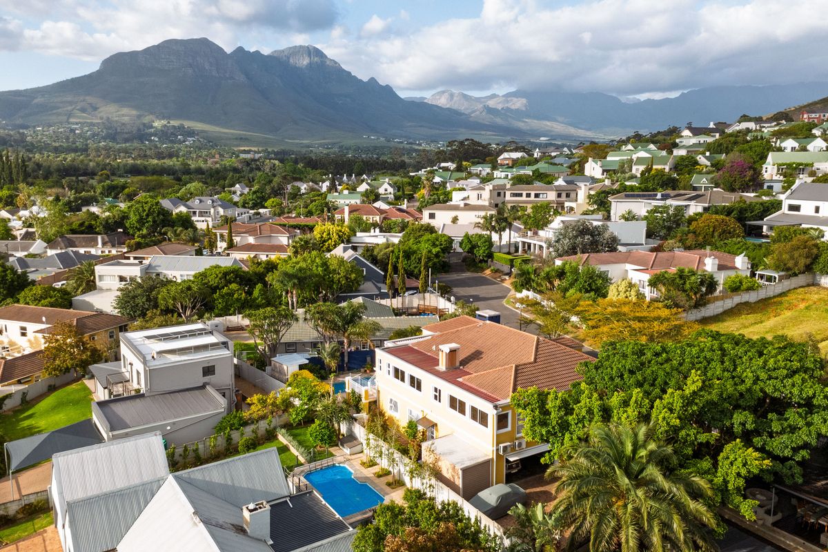 An elevated aerial view of the residential property, showcasing the swimming pool, roof structure, and surrounding neighbourhood with mountain views.