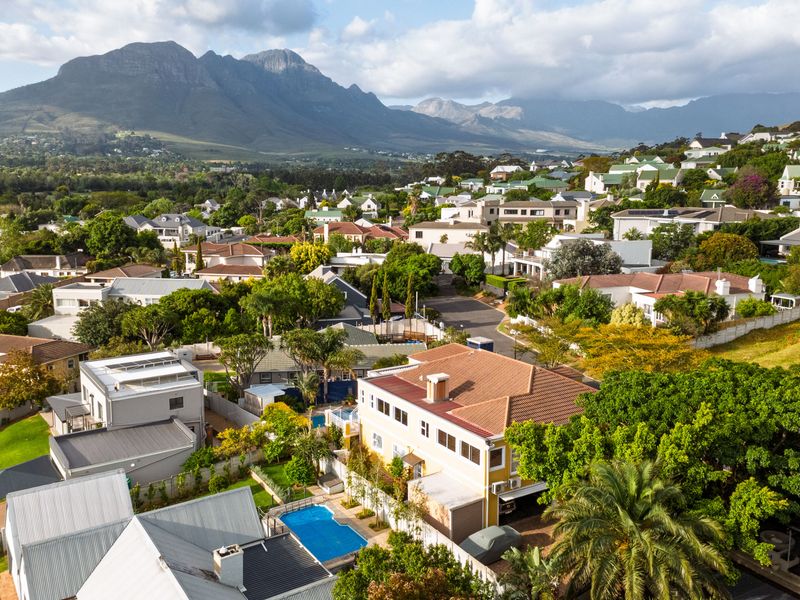 An elevated aerial view of the residential property, showcasing the swimming pool, roof structure, and surrounding neighbourhood with mountain views.