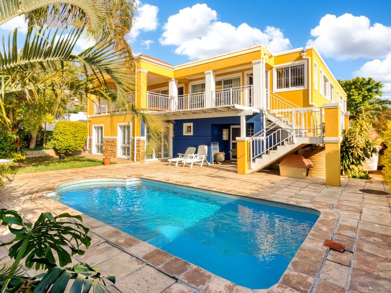 Rear exterior view featuring a swimming pool, stone-paved patio, and a two-story house with a balcony and external staircase.