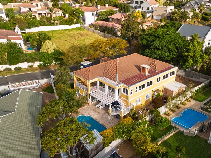 Aerial view of a two-story residential property featuring a swimming pool, tiled roof, and rear balcony set within a landscaped suburban garden.