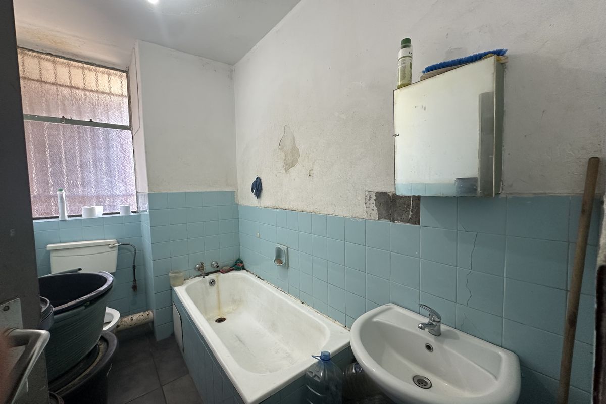A dated bathroom featuring a pedestal basin, bathtub, and toilet, requiring significant cosmetic renovation and repair to wall finishes.