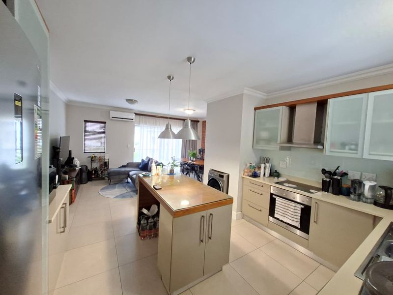 Spacious open-plan living area featuring a modern kitchen with a central island, built-in appliances, and tiled flooring, seamlessly flowing into the lounge and dining space.