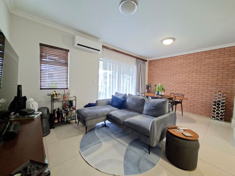 Open-plan living and dining area featuring a distinctive exposed brick feature wall, tiled flooring, and a split-system air conditioner for climate control.