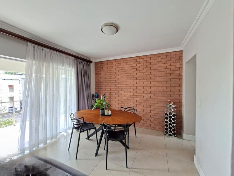 Dining area featuring a distinctive exposed brick feature wall, neutral tiled flooring, and large sliding glass doors providing access to the balcony.