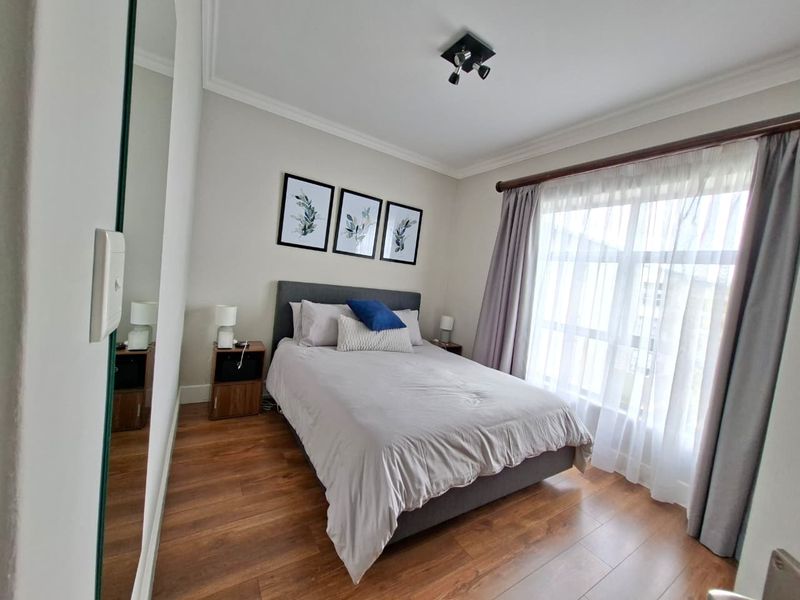 A well-maintained bedroom featuring laminate flooring, ceiling coving, and a large wall mirror, offering a clean and comfortable living space.