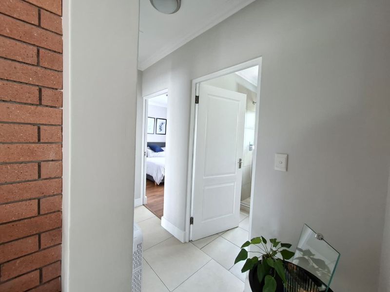 A clean, neutral hallway featuring tiled flooring and an exposed brick accent wall, providing access to adjacent bedrooms and bathrooms.