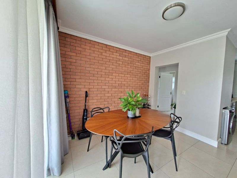 A dining area featuring a prominent exposed brick feature wall, neutral tiled flooring, and crown molding, providing a warm and textured aesthetic.