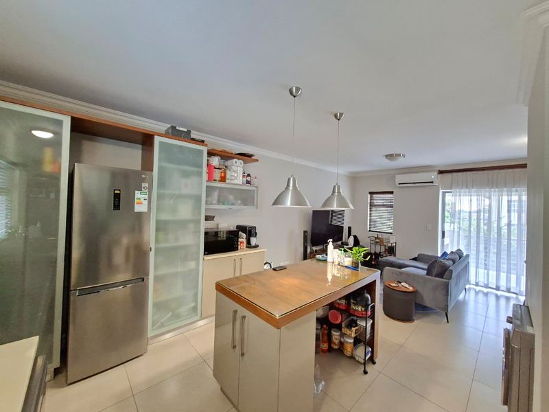 Open-plan living area featuring a modern kitchen with a central island, tiled flooring, and a split-system air conditioner, flowing into the lounge space.