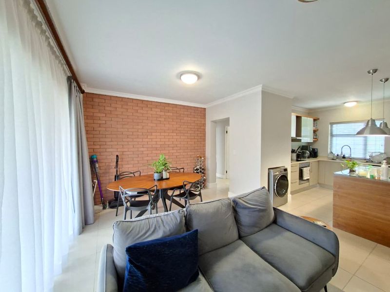 Open-plan living and kitchen area featuring an exposed brick feature wall, modern cabinetry, kitchen island, and tiled flooring throughout.