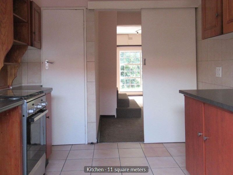 A functional kitchen featuring wooden cabinetry, laminate countertops, and tiled flooring, with a sliding door leading to an adjacent living area.