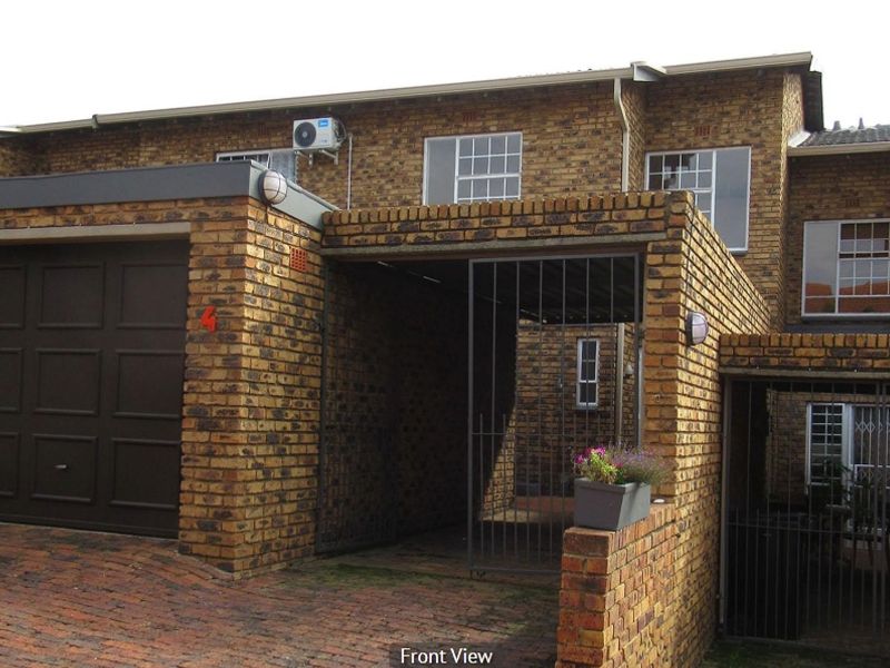 Front elevation of a face brick townhouse featuring a garage, secure gated entrance, and paved driveway area.