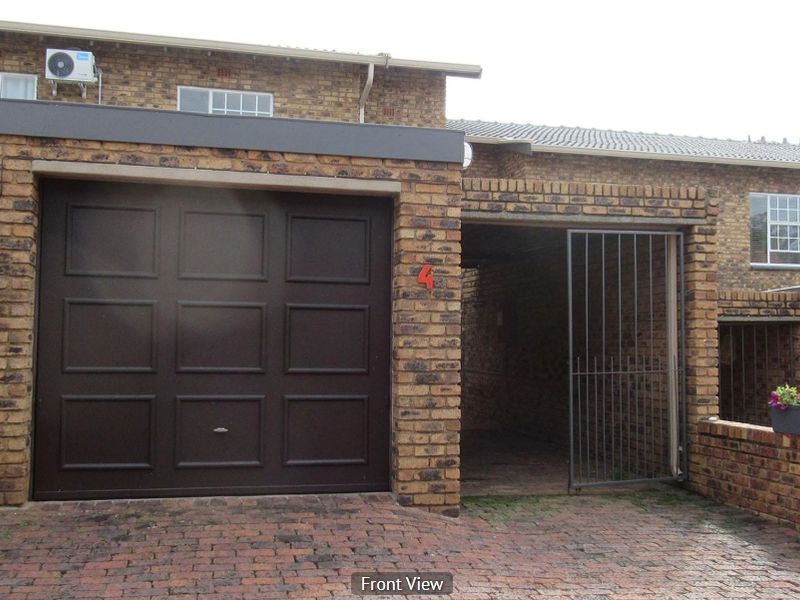 Front elevation of a brick townhouse featuring a single garage, secure gated entrance, and paved driveway area.