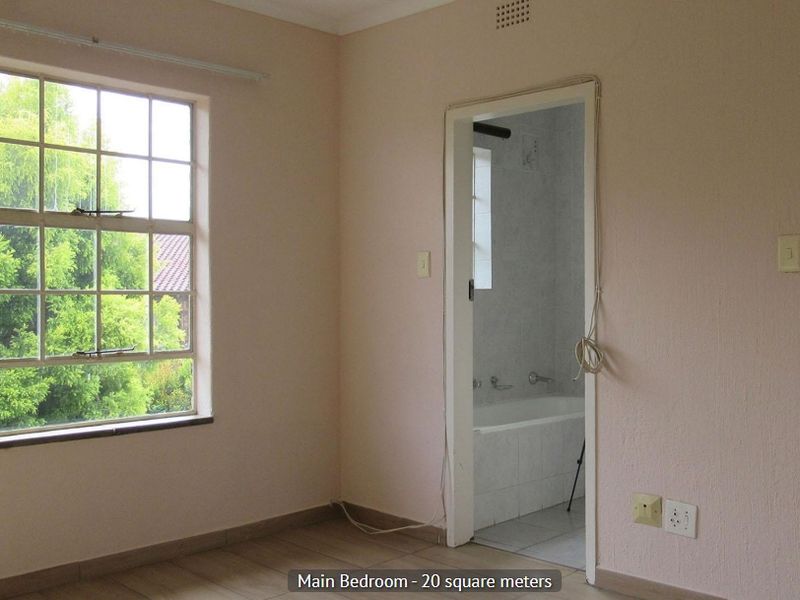 An empty bedroom featuring tiled flooring, a large multi-pane window, and direct access to an en-suite bathroom.