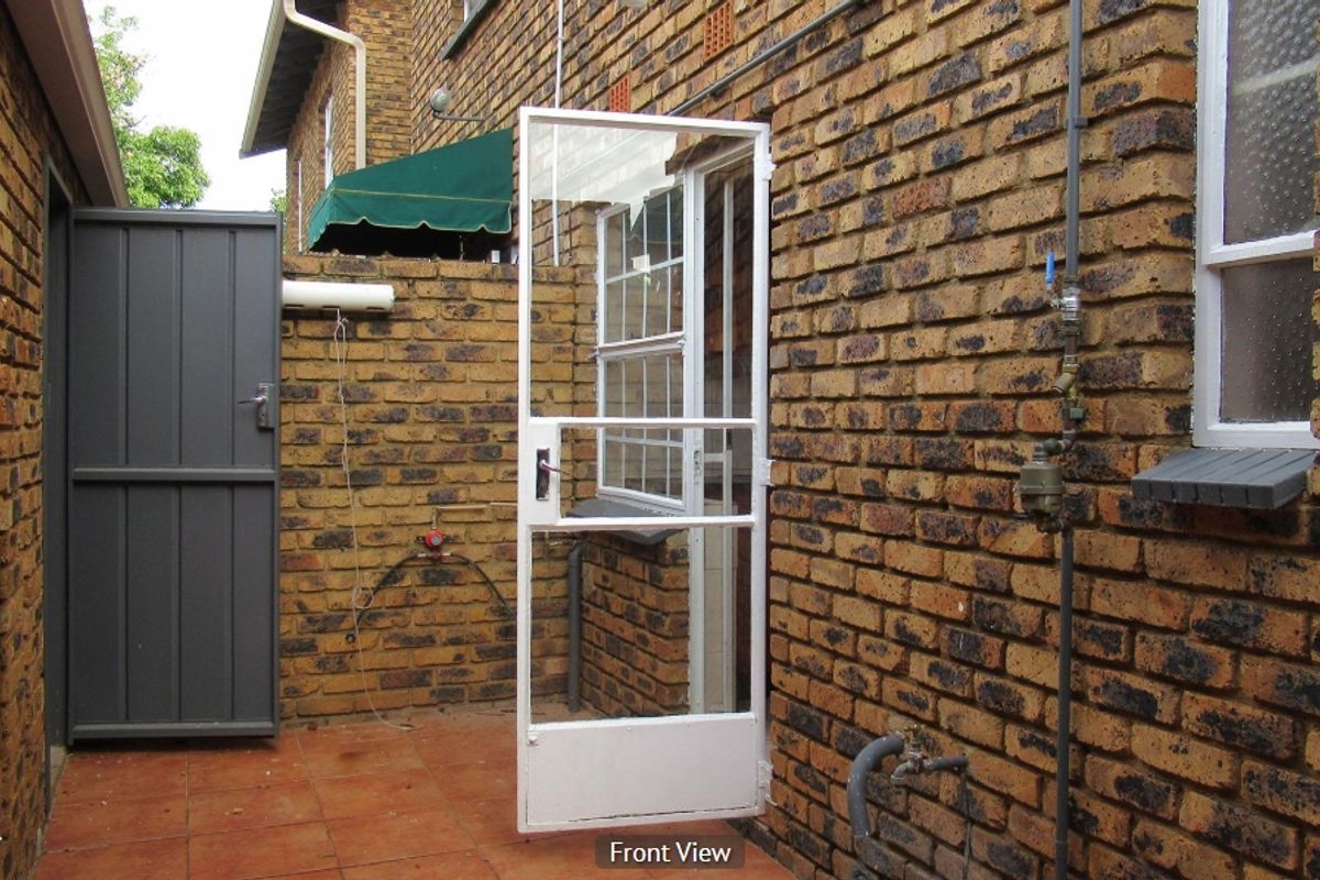 A rear exterior view of a townhouse featuring a tiled patio area, face brick walls, and a white security gate.