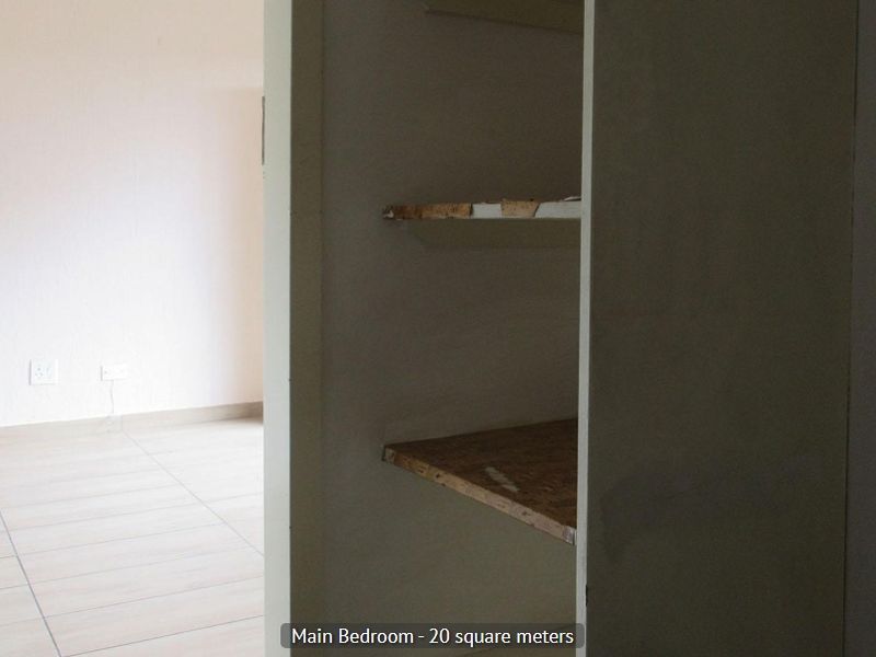 An empty bedroom featuring tiled flooring and built-in shelving with visible wear on the shelf edges.