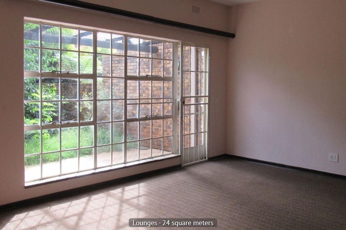 Spacious living area featuring large steel-framed windows, a security gate, and carpeted flooring, offering direct access to the outdoor patio area.