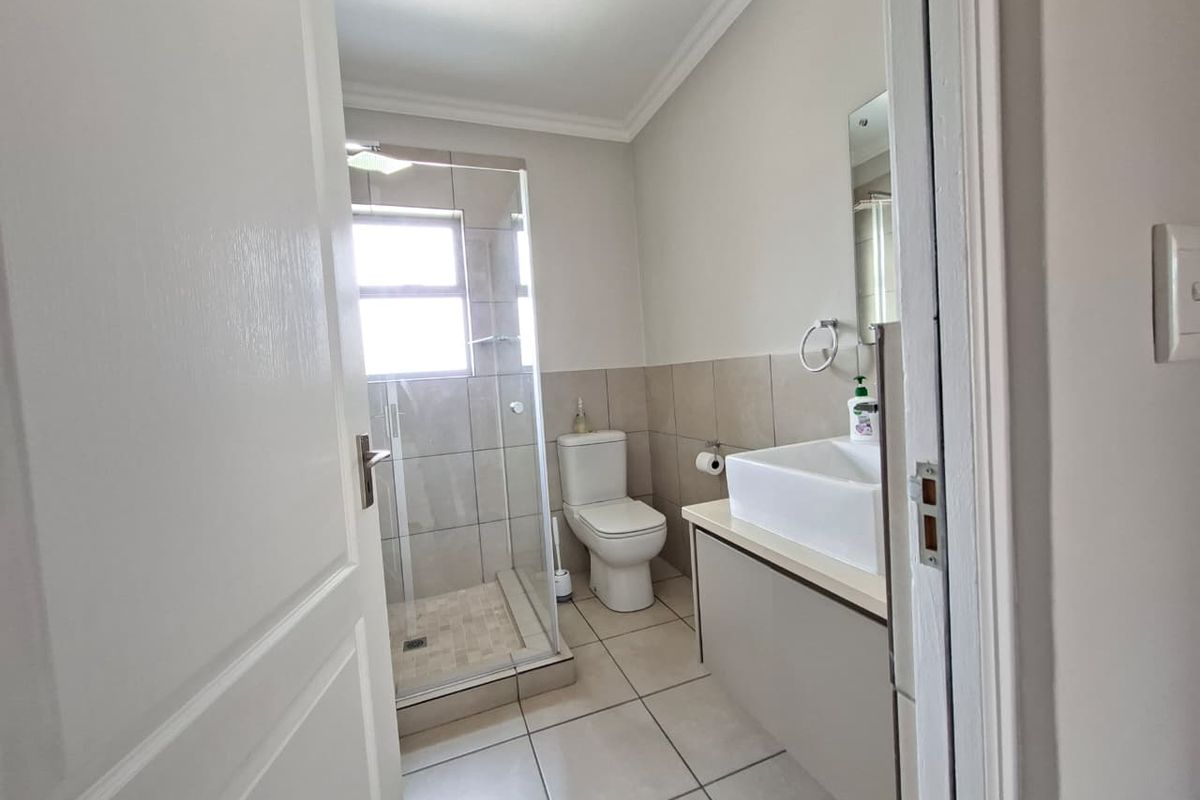 A clean and modern bathroom featuring a glass-enclosed shower, a contemporary vessel sink vanity, and neutral floor-to-ceiling tiling.