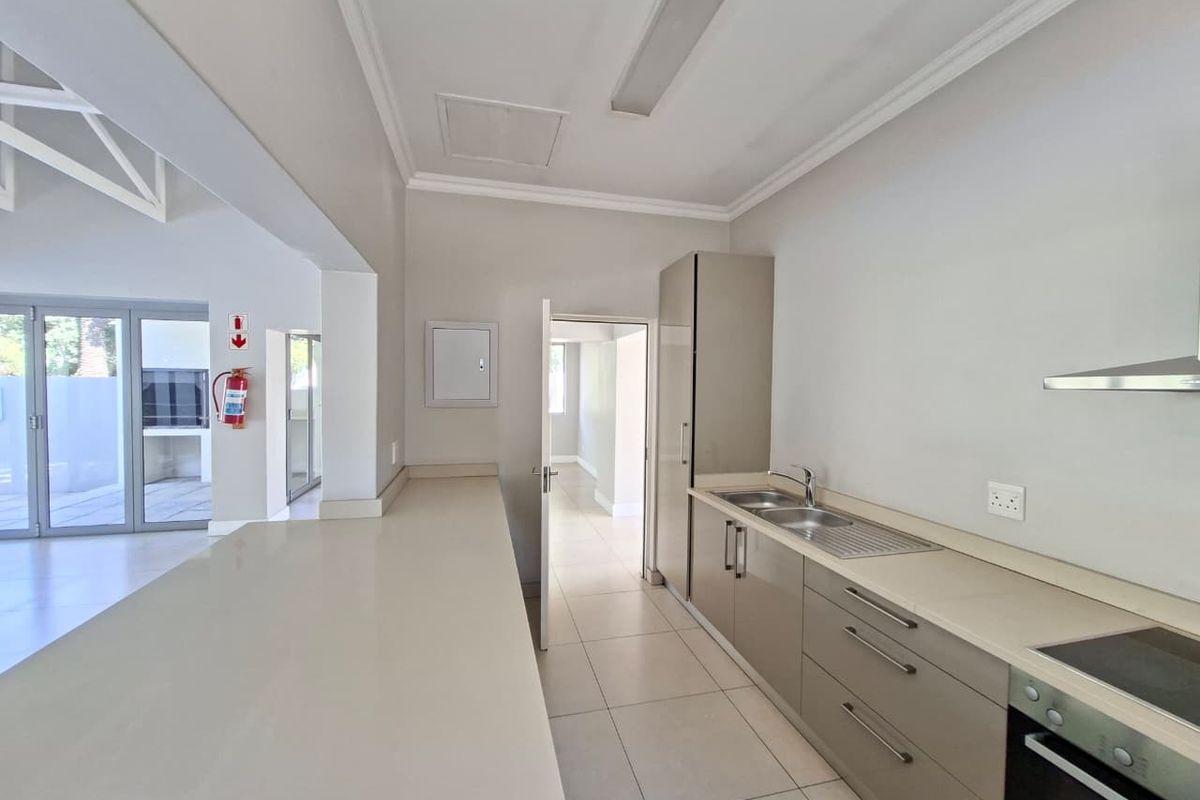 Modern kitchen featuring sleek cabinetry, stone countertops, integrated appliances, and tiled flooring, leading into an open-plan living area with patio access.