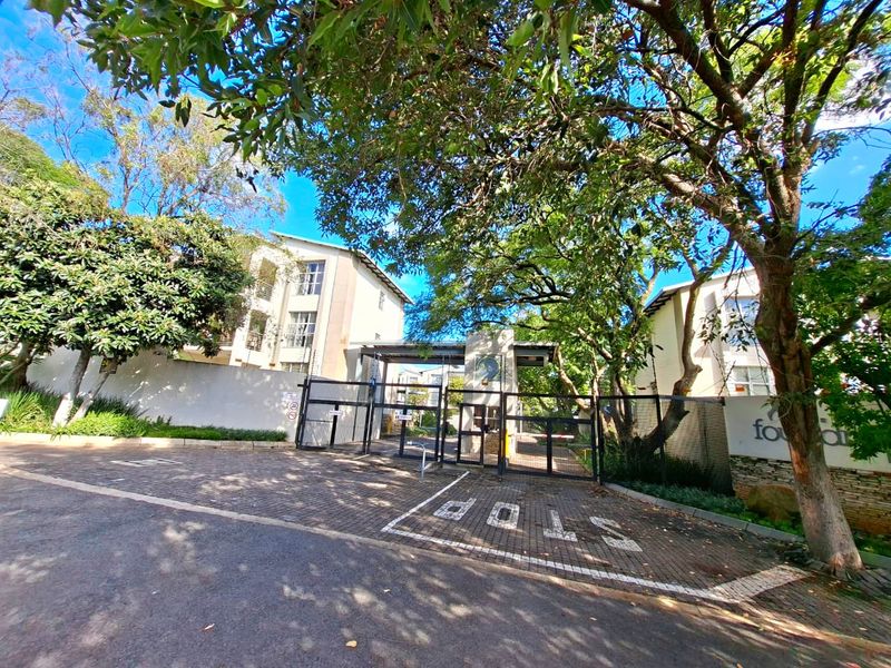 Street view of the apartment complex entrance featuring a secure gated access point and paved driveway surrounded by mature trees.