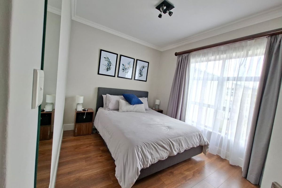 A well-maintained bedroom featuring laminate flooring, ceiling coving, and a large wall mirror, offering a clean and comfortable living space.