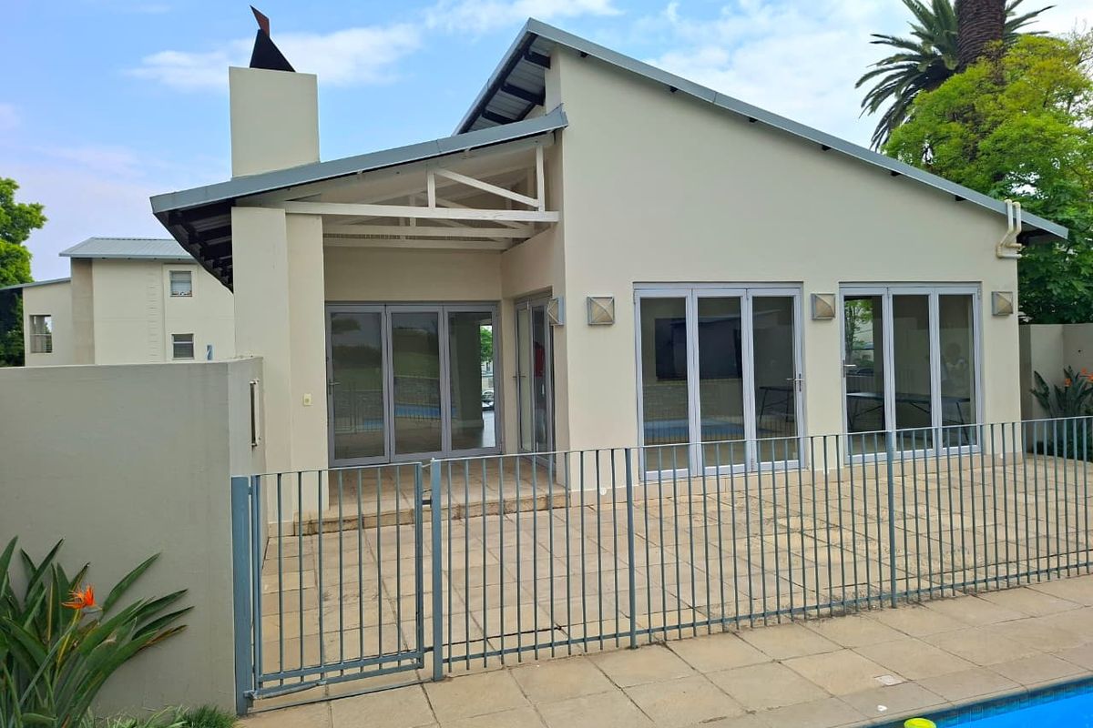 Rear view of the property featuring a paved patio area, modern bi-fold doors, and a swimming pool with metal perimeter fencing.